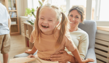 young girl smiling wearing pig tails sitting on moms lap